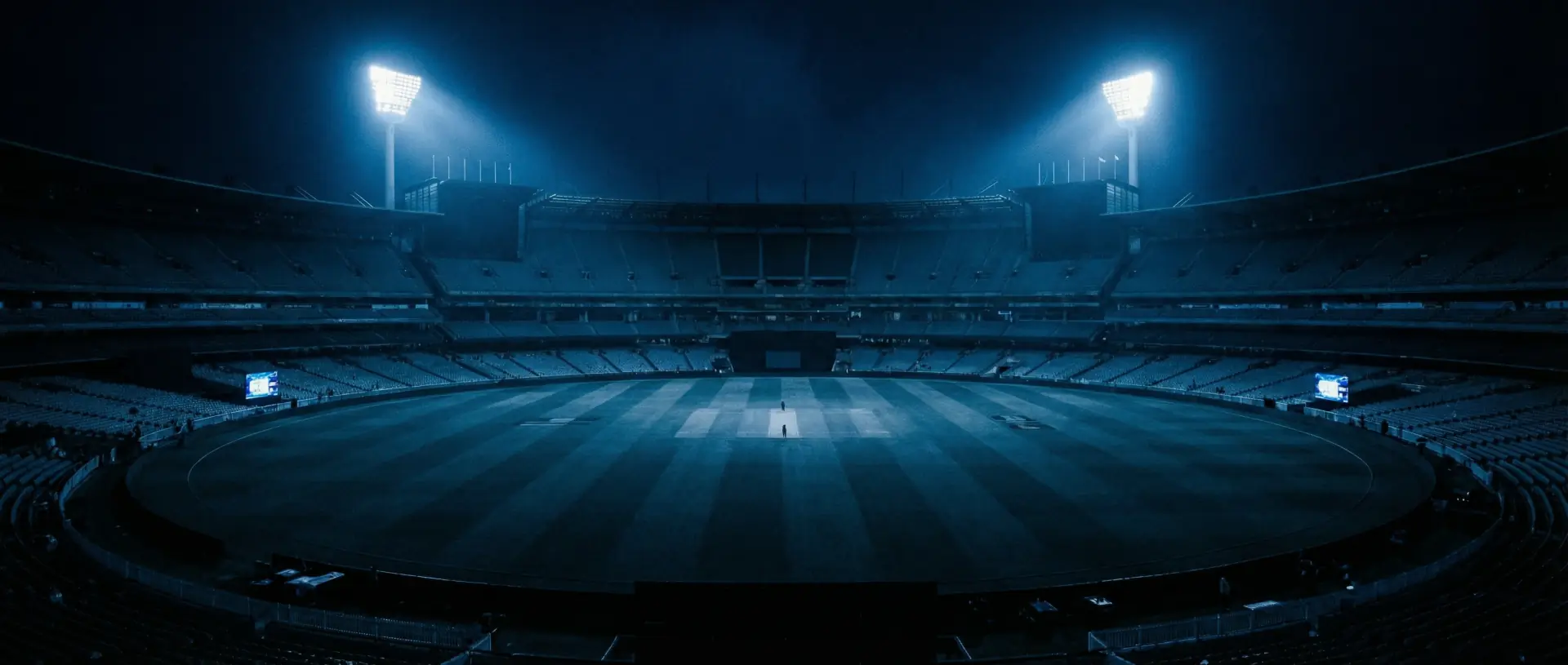 Night cricket stadium with wide cinematic framing and blue lighting.